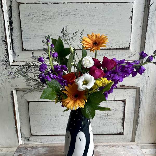 Mixed bouquet with orange gerberas, purple flowers, and roses in a black vase