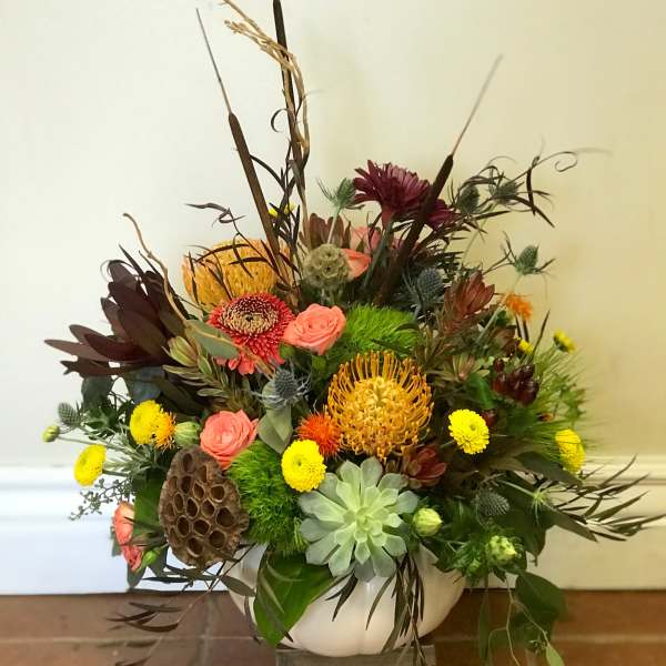 Mixed floral arrangement in a white bowl vase with tall dried accents