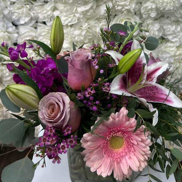 Pink and purple mixed bouquet with lilies, roses, and a gerbera daisy in a glass vase