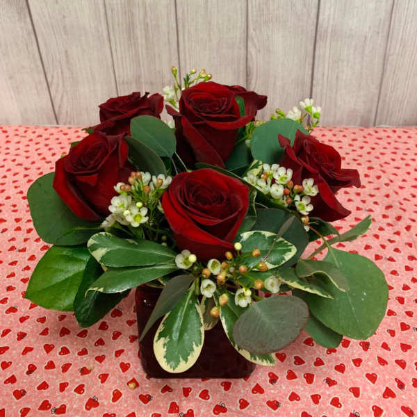 Red roses arranged in a low vase with mixed greenery and small white filler flowers