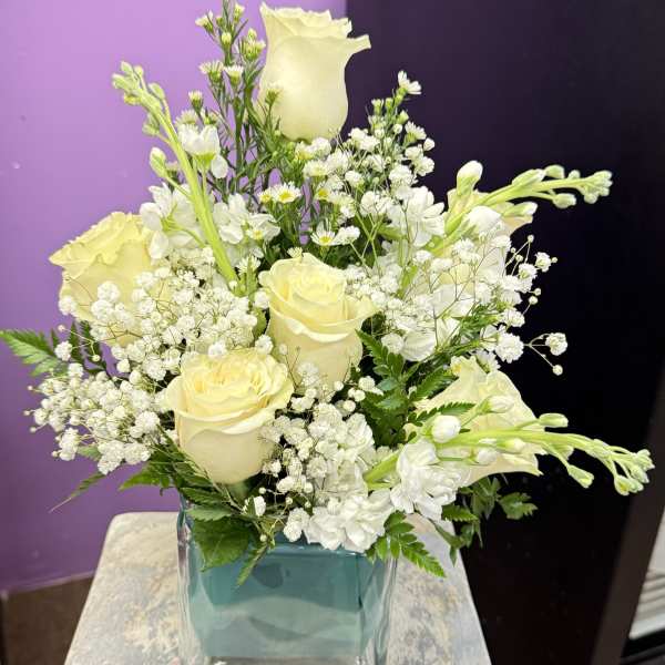 White roses and small white flowers arranged in a square glass vase