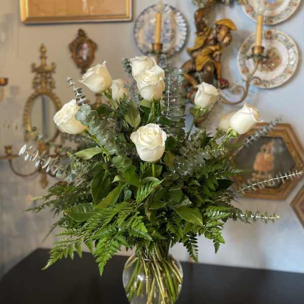 White roses arranged in a clear glass vase with greenery