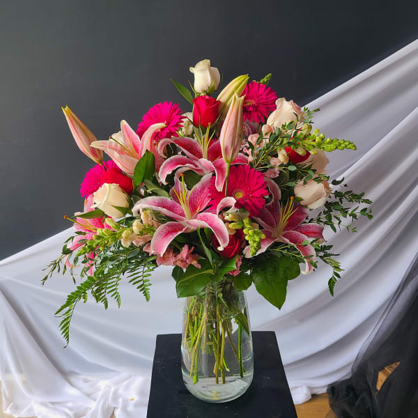 Pink lilies and roses in a glass vase with bright pink daisies