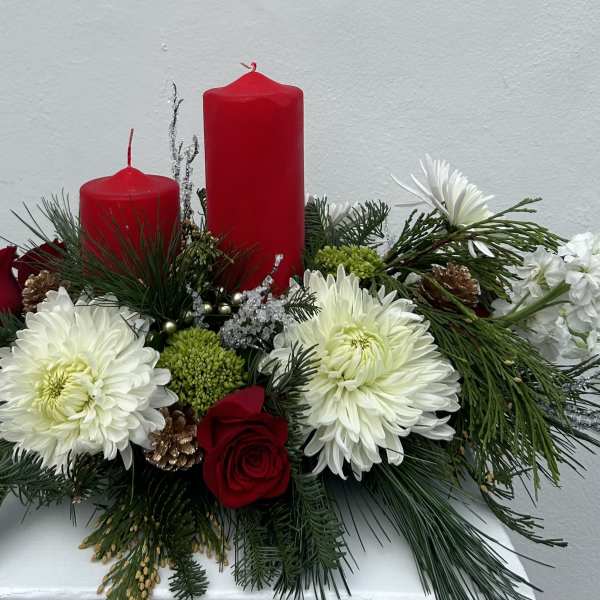 Red candles in a floral arrangement with white blooms and evergreen accents