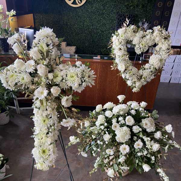 White floral funeral sprays and a heart-shaped wreath on stands