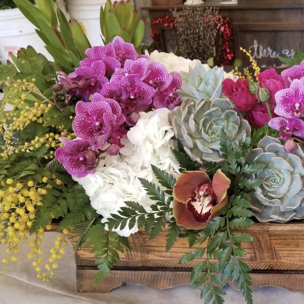 Mixed floral arrangement in a wooden box with orchids, roses, and succulents