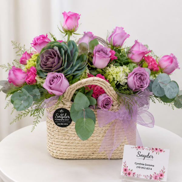 Pink and lavender roses arranged in a woven basket with a ribbon