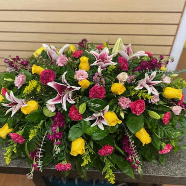 Large mixed floral arrangement with yellow roses, pink carnations, and lilies