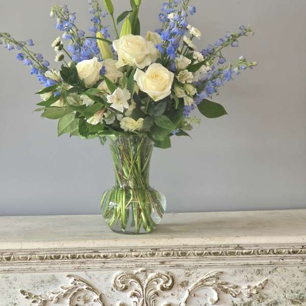 White roses and blue delphinium in a clear glass vase