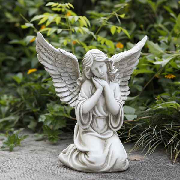 White angel statue kneeling with folded hands in a garden setting