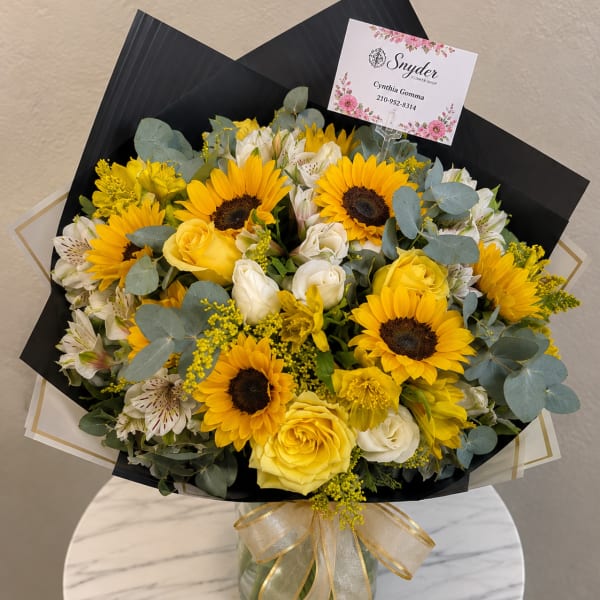 Bouquet of yellow sunflowers, yellow and white roses, and white alstroemeria in a glass vase