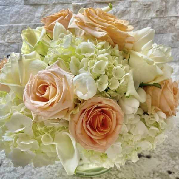 Bouquet of peach roses, white hydrangeas, and white calla lilies in a glass vase
