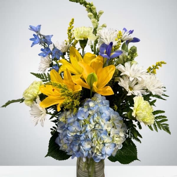Bouquet of yellow lilies, blue hydrangea, and white daisies in a glass vase