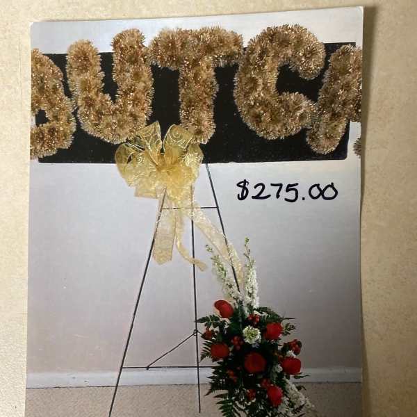Gold tinsel letters on an easel with a red floral spray below