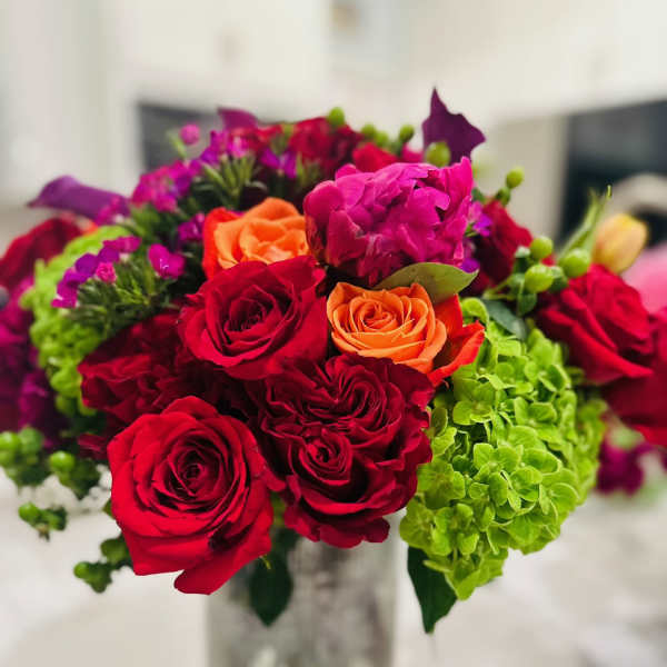 Bouquet of red and orange roses with green hydrangeas in a glass vase