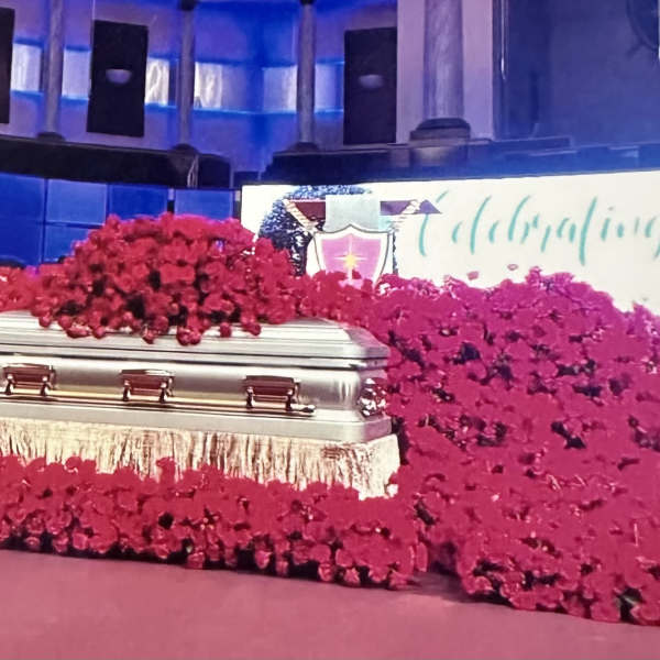 Silver casket surrounded by large red floral sprays