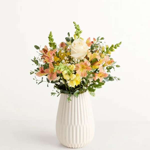 Mixed bouquet of peach and yellow flowers in a white vase