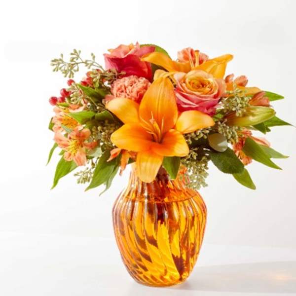 Orange and pink mixed bouquet in an amber glass vase