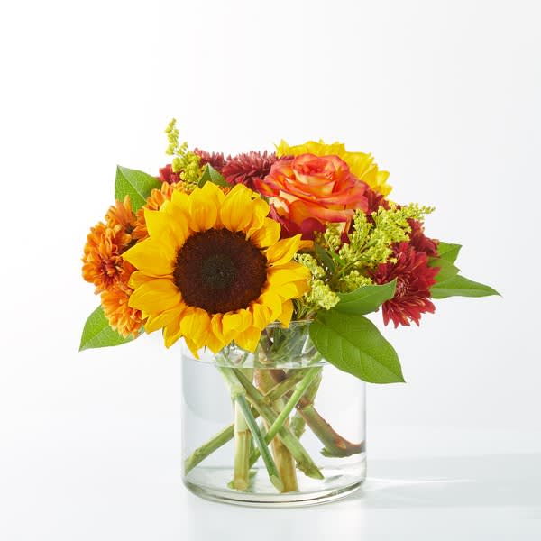 Sunflower and mixed autumn flowers in a clear glass vase