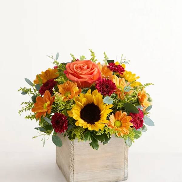 Bright mixed bouquet in a square wooden box with a sunflower and orange rose