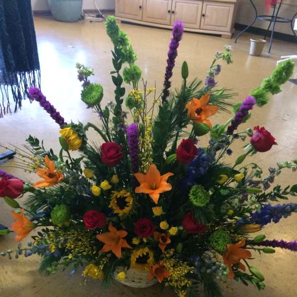 Large mixed flower arrangement in a white basket with orange lilies and red roses