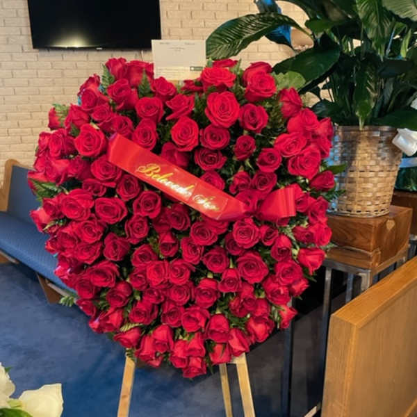 Large heart-shaped arrangement of red roses on an easel with a ribbon