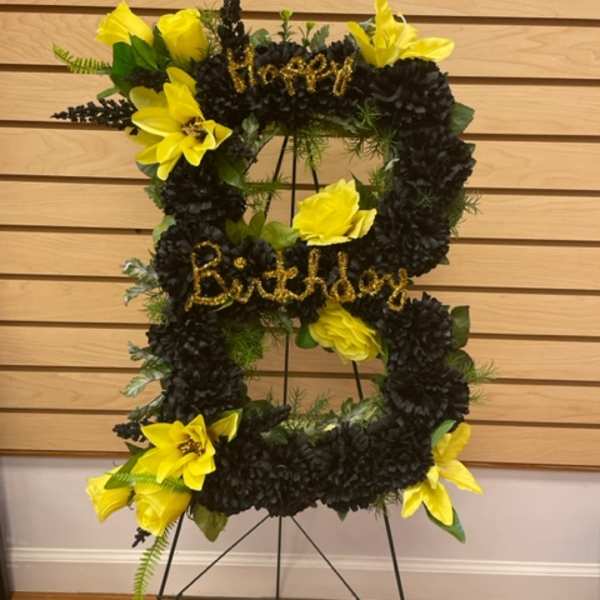 Black and yellow floral standing wreath on an easel with birthday lettering