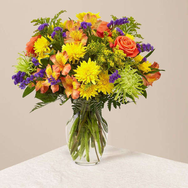 Mixed bouquet of yellow, orange, and purple flowers in a glass vase