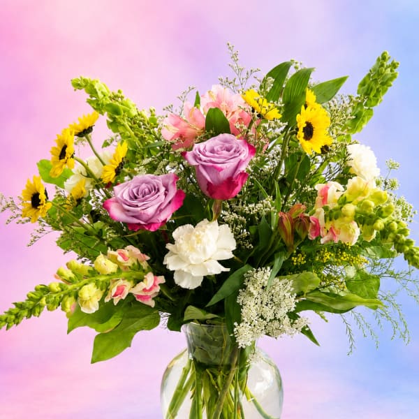 Mixed bouquet of roses, sunflowers, and lilies in a glass vase