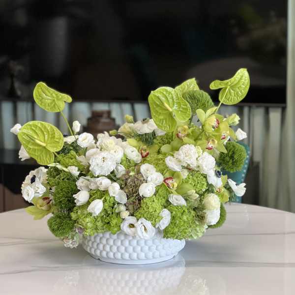 Green and white floral arrangement in a white textured bowl vase