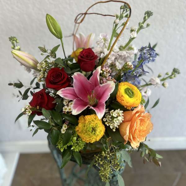 Mixed bouquet with red roses, pink lily, and yellow ranunculus in a basket