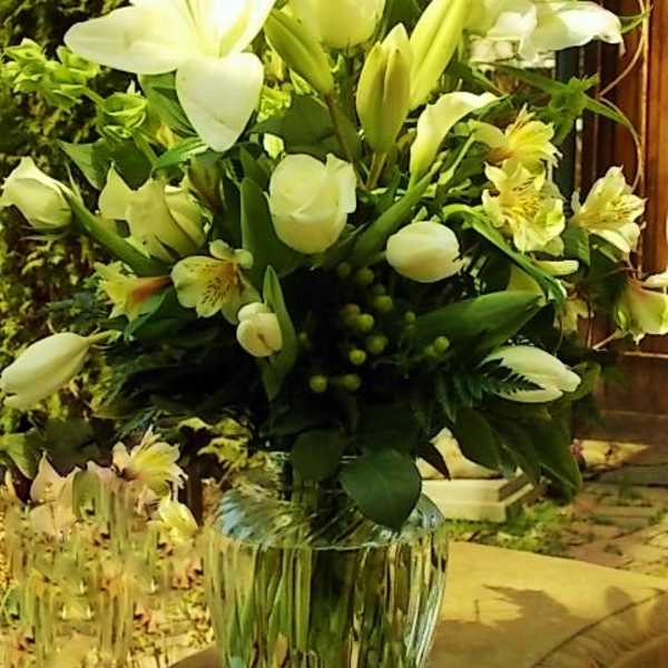 White lilies and pale yellow flowers arranged in a clear glass vase.