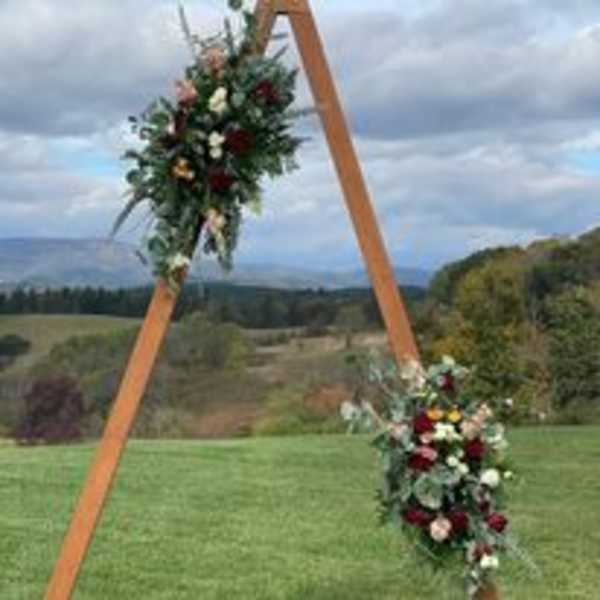 Two floral arrangements on a wooden arch outdoors