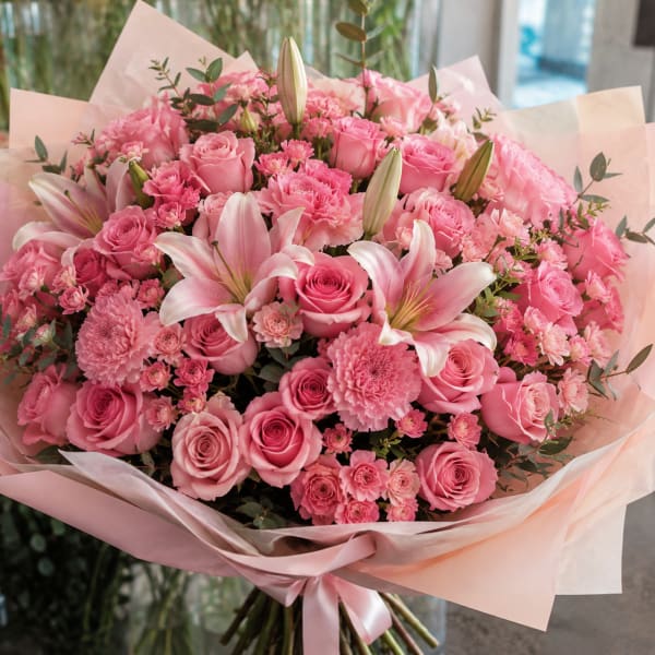 Large pink bouquet of roses, lilies, and carnations wrapped in pale paper