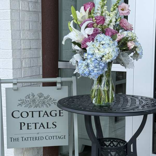Mixed bouquet in a clear glass vase with lilies, roses, and blue hydrangeas