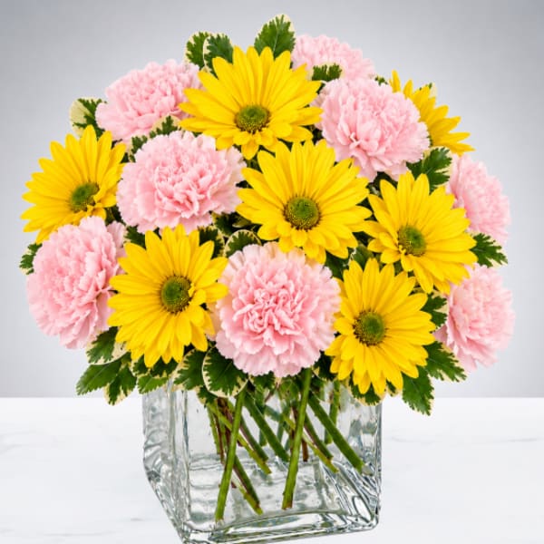 Pink carnations and yellow daisies arranged in a clear glass vase