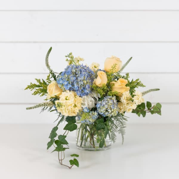 Blue hydrangeas and pale yellow roses in a clear glass vase