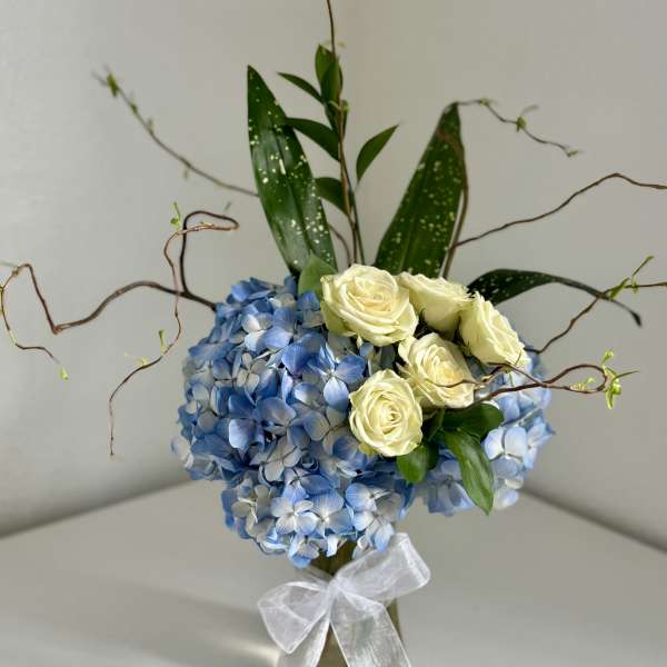 Blue hydrangea arrangement with cream roses in a glass vase