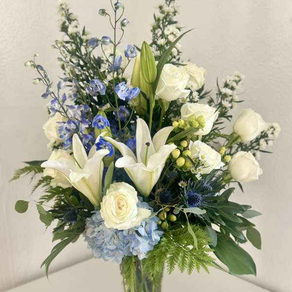 White lilies, roses, and blue flowers in a clear glass vase