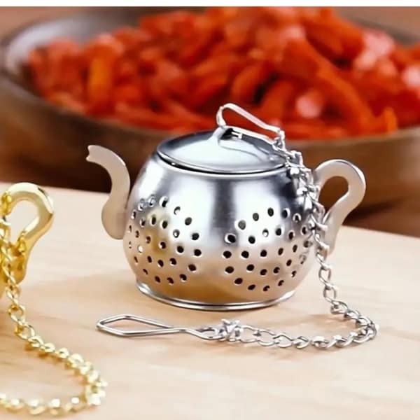 Metal tea infuser with a chain and lid on a wooden surface