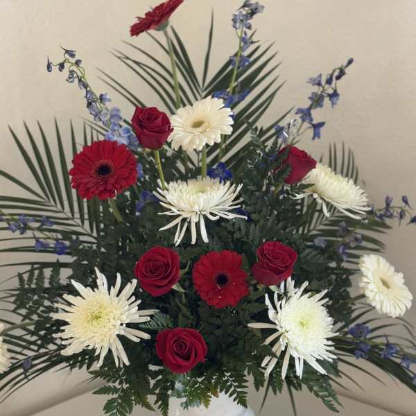 Red roses and white daisies in a white vase with blue accents