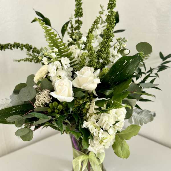 White roses and hydrangeas in a glass vase with mixed greenery