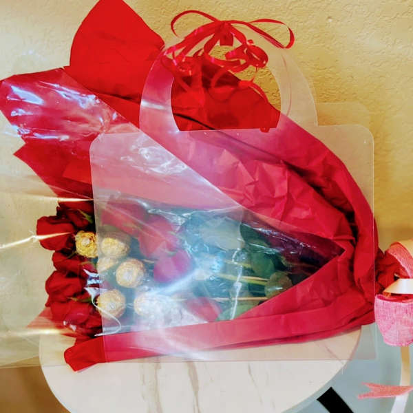 Red rose bouquet wrapped in red and clear plastic with a pink ribbon