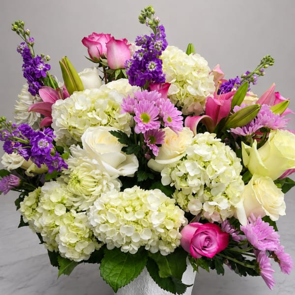 Mixed bouquet of pink, white, and purple flowers in a white vase