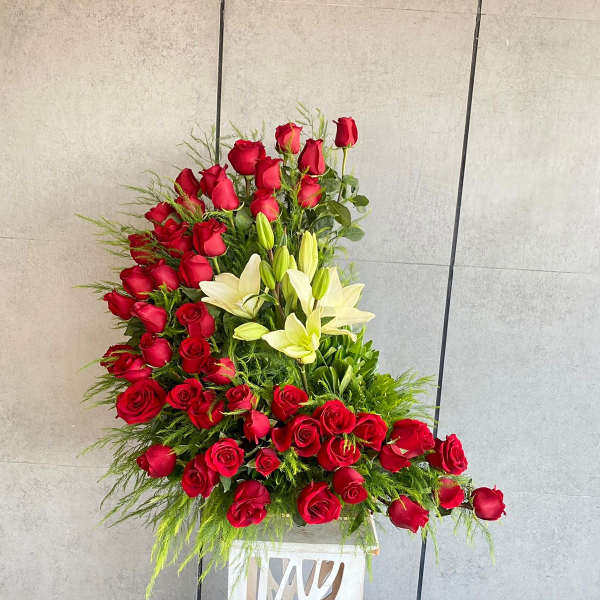 Large red rose and white lily arrangement in a white pedestal vase