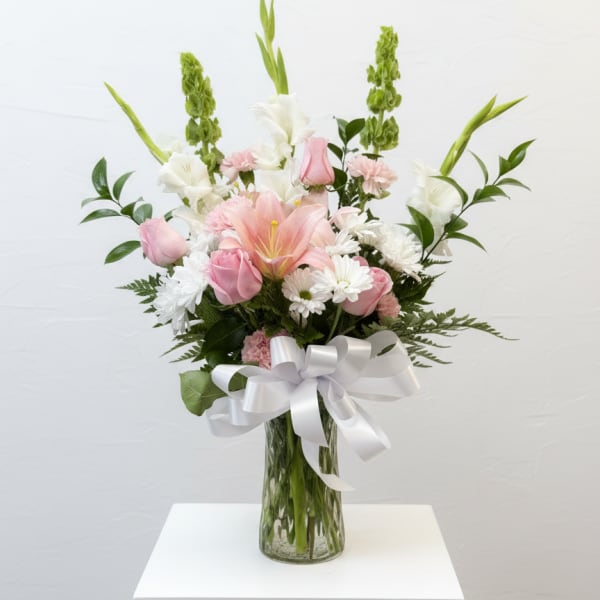 Pink and white flower arrangement in a glass vase with a white ribbon