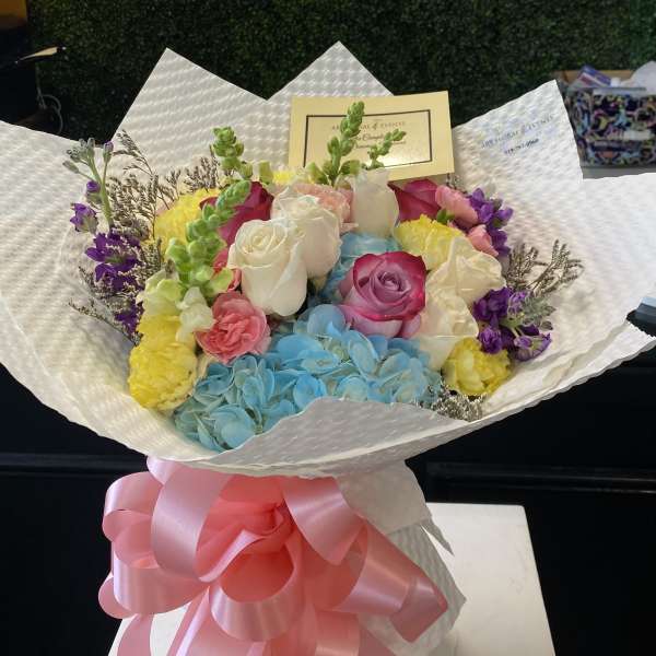 Colorful bouquet of roses, hydrangeas, and carnations wrapped in white paper with a pink bow