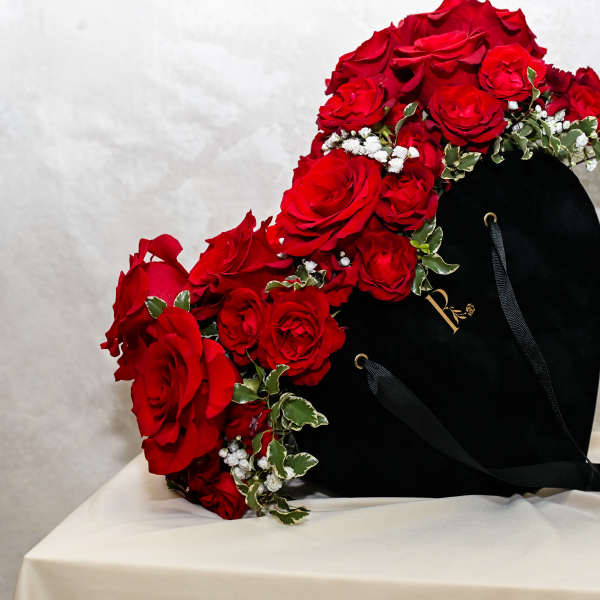 Heart-shaped black box topped with red roses and small white flowers