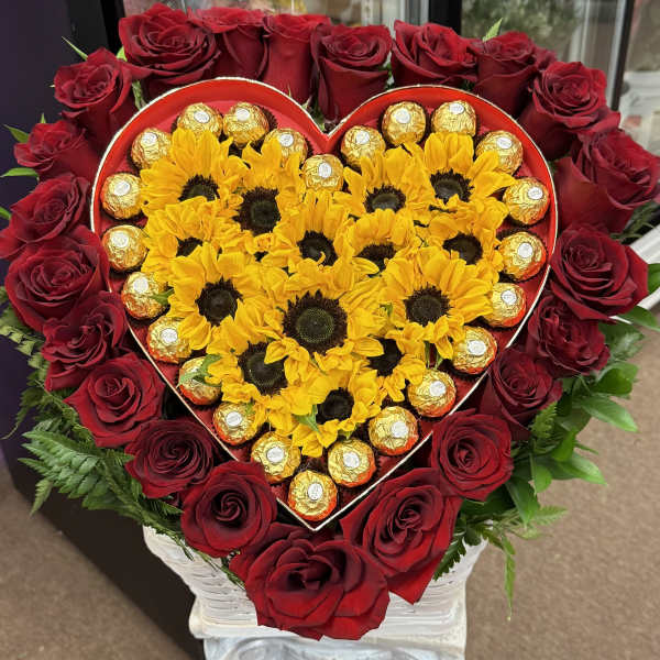 Heart-shaped arrangement of red roses, yellow sunflowers, and gold-wrapped chocolates