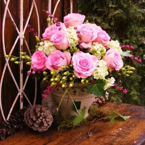 Pink roses arranged in a decorative vase with pinecones nearby
